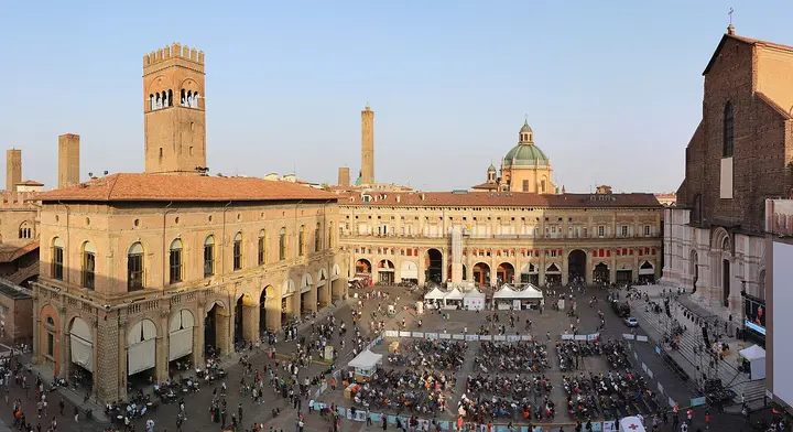 Crowds in Piazza Maggiore beneath the towers and arcades of Bologna.