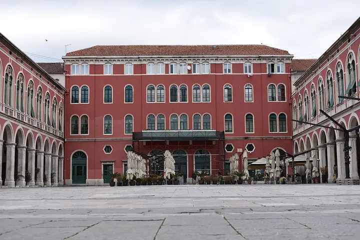 Open square enclosed by red buildings and arcades in Split.
